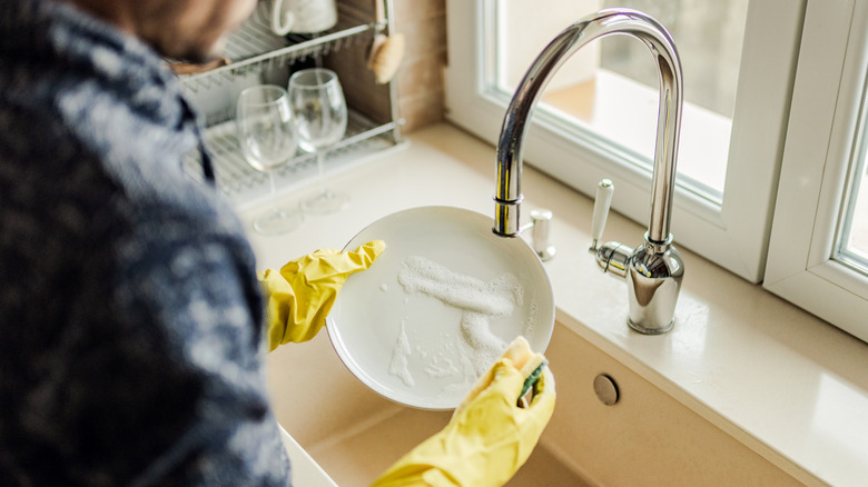 A man washing a white ceramic plate in a kitchen sink