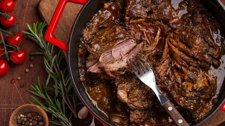 Pot roast in a red Dutch oven with tomatoes and peppercorns