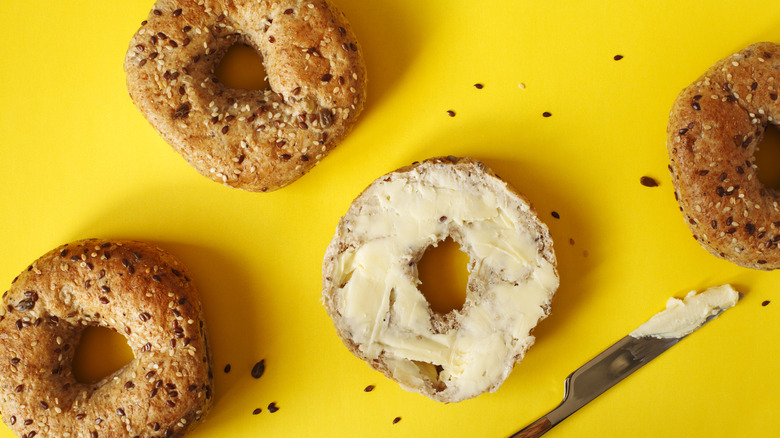 Bagels and knife with cream cheese on yellow background