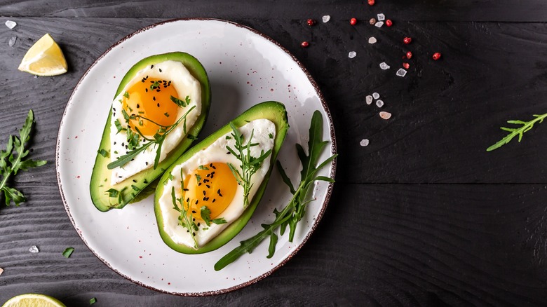 egg baked into an avocado with herbs and slice of lemon