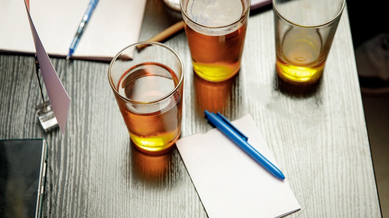Three glasses of beer surround a notepad and pen