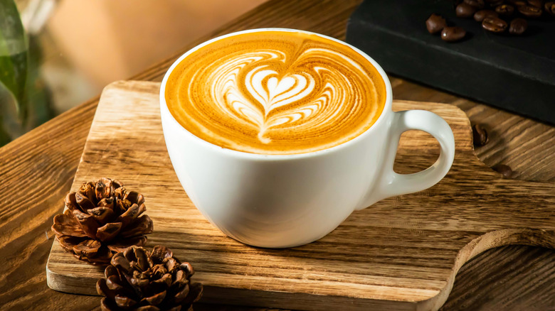 latte with latte art and two mini pinecones on a wooden board