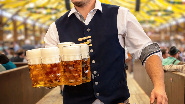 Munich beer hall with patrons on either side of a male server holding several brews in large, glass steins