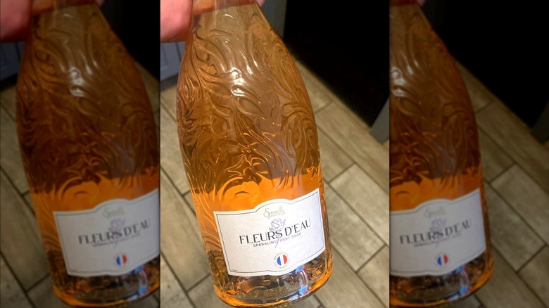 A hand holding a bottle of sparkling rosé wine