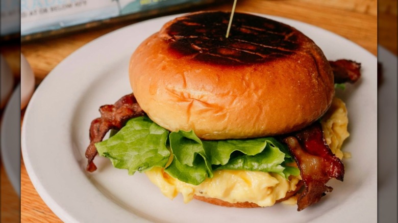 Egg and bacon on a grilled bun sandwich on white plate
