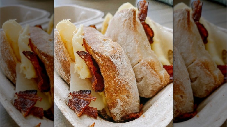 Scrambled eggs, swiss cheese, and bacon on a ciabattina bread sandwich in a to-go box