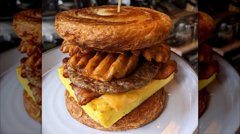 bacon, sausage, egg, cheese, and waffle fries in between two danishes on a white plate