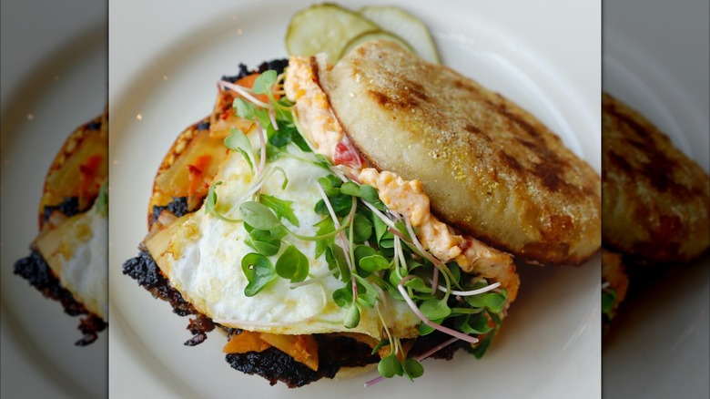 English muffin with egg, chorizo, kimchi, and pimento cheese on white plate