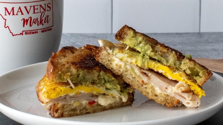 Sandwich with eggs, avocado, and ham on white plate