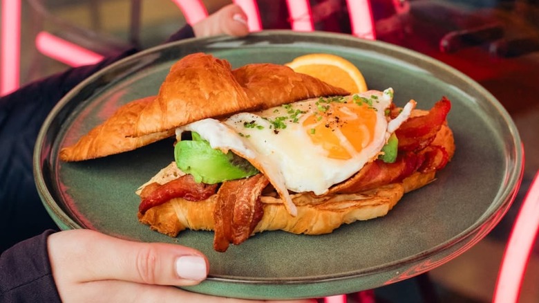 Croissant sandwich with bacon, egg, and avocado