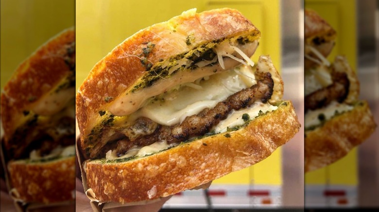 Hand holding a sourdough bread sandwich with sausage, pesto, eggs, and cheese