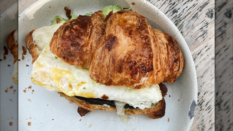 Egg sandwich on a croissant on a plate on wooden table