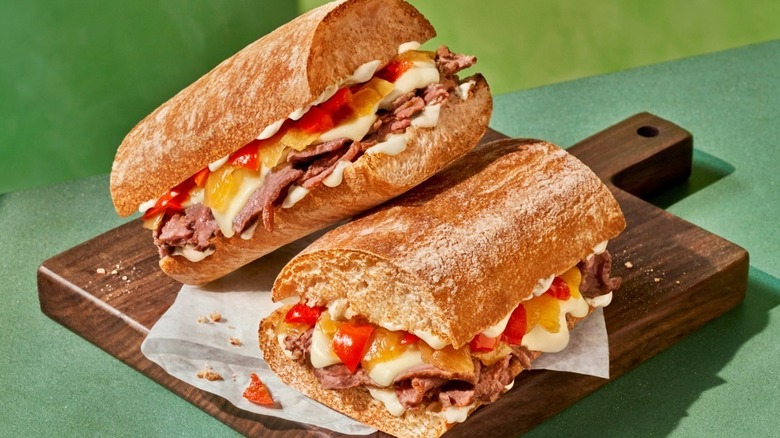 Two halves of a Ciabatta Cheesesteak sandwich from Panera Bread on a wooden board