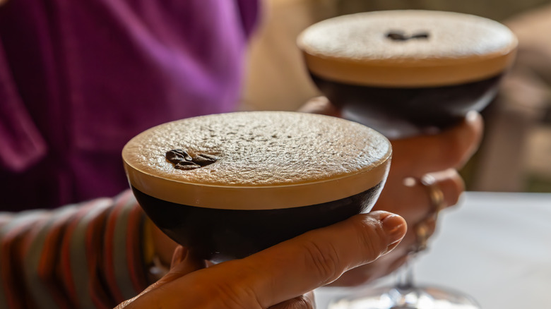 A close up of two hands holding espresso martinis