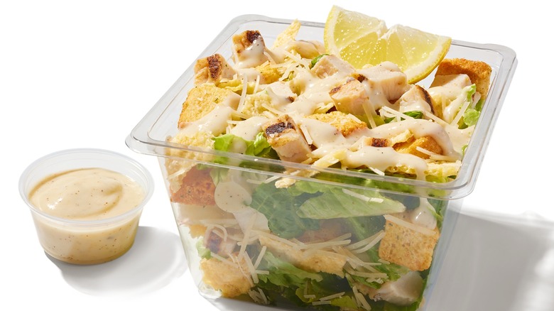 Plastic container of chicken Caesar salad with dip on the side