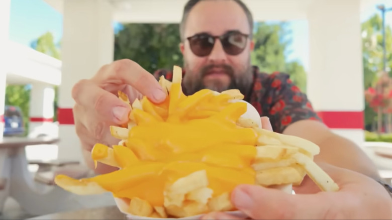 a bearded man holds a basket of cheese-covered In-N-Out fries up to the camera.