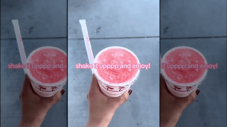 a hand with painted fingernails holds a closed In-N-Out cup with bubbly pink liquid under the lid.