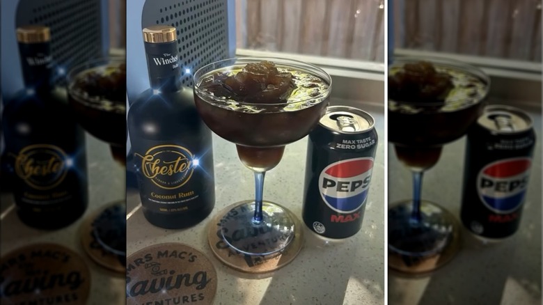 Margarita glass with icy brown drink next to coconut rum and Pepsi can