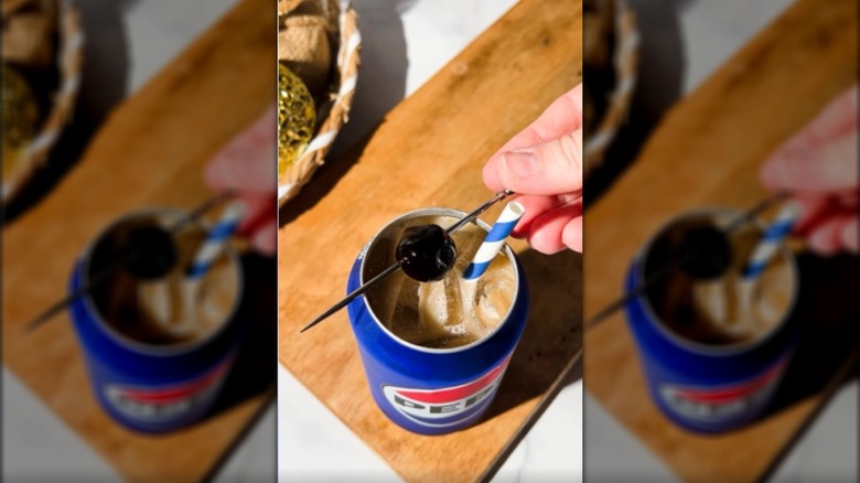 Top view of pepsi can filled with icy drink with straw and skewered cherry