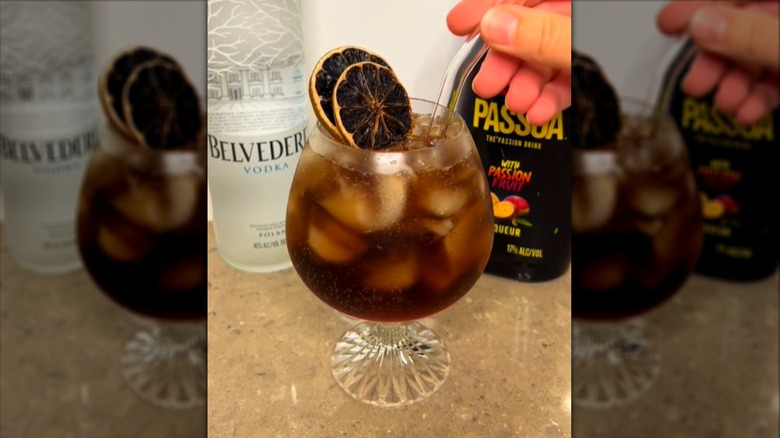 brown drink over ice in goblet with dried lime slices