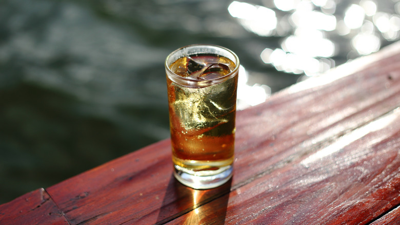 Brown drink on ice in tall glass by water