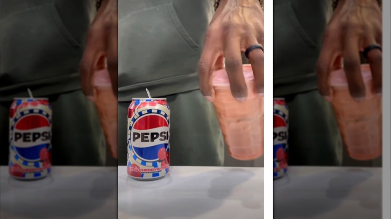 A woman's hand shaking a cup with a dirty Pepsi next to a can of cherry Pepsi
