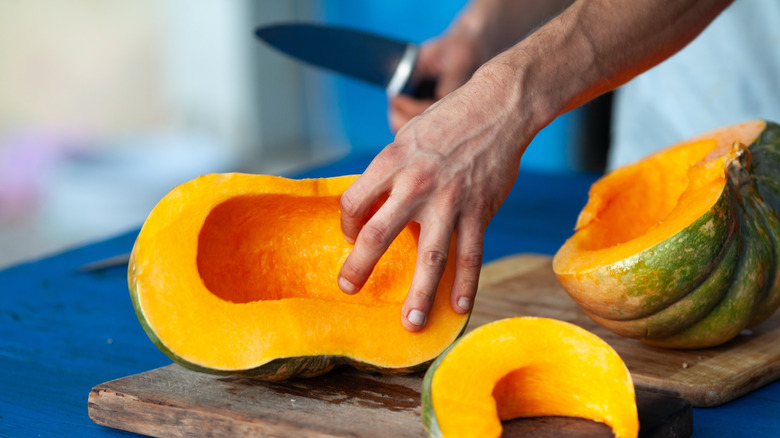 A person is cutting a pumpkin on a wooden cutting board.