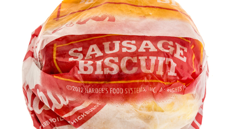 A Hardee's sausage biscuit wrapped in branded paper on a white background