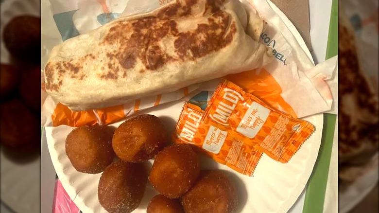 A grilled burrito and a side of Cinnabon Deights on a paper plate with hot sauce packets