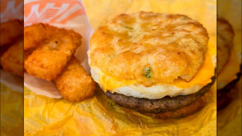 A jalapeno cheddar biscuit breakfast sandwich and a side of hashbrowns on yellow paper