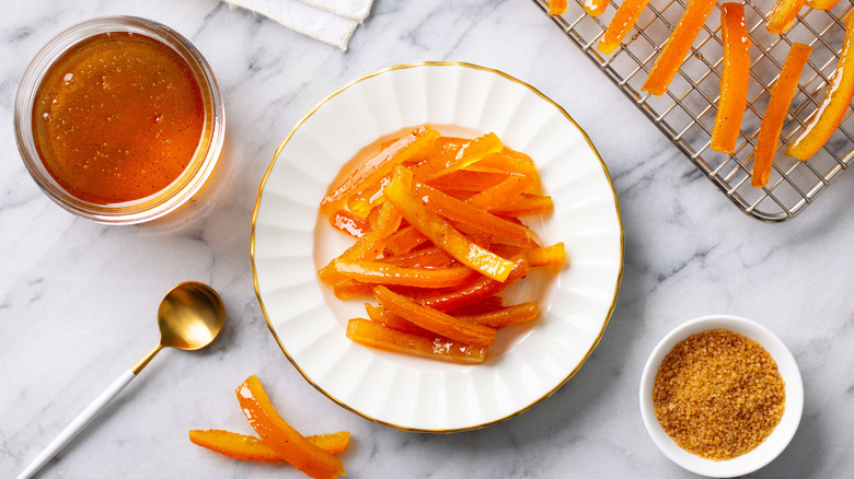 Candied orange peels on a white plate with orange marmalade and a bowl of brown sugar on the side