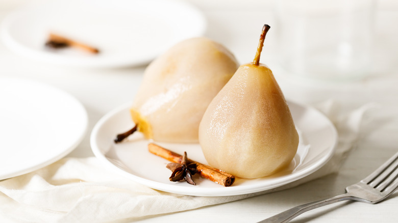 Poached pears on a white plate with a cinnamon stick and star anise