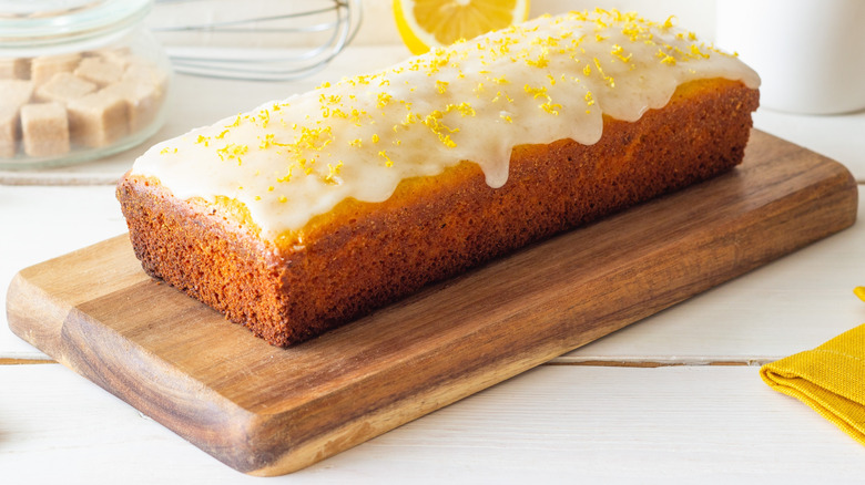 A lemon loaf cake topped with lemon glaze on a wooden board