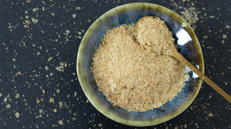 A bowl full of nutritional yeast with a spoon on a table