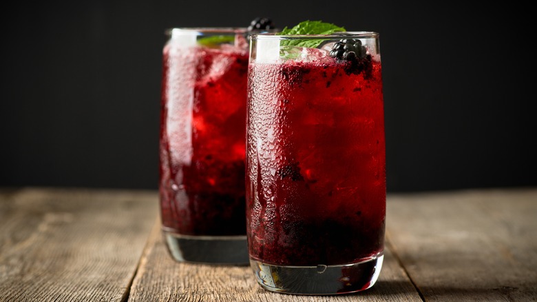 Two deep red drinks garnished with blackberry and mint