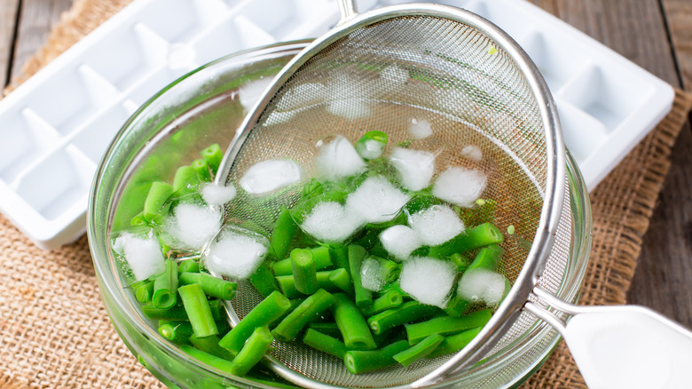 Blanched green beans being dunked into a waiting ice bath