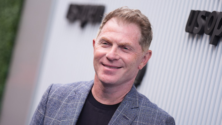 Headshot of Food Network celebrity chef Bobby Flay smiling in front of a light-colored background.