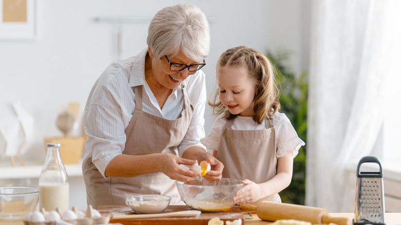 Grandma cracking egg and baking with young granddaughter