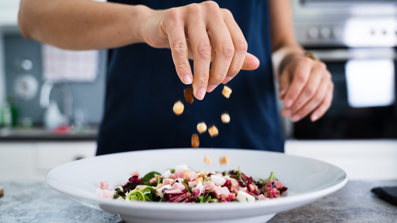 sprinkling toppings on salad in white platter