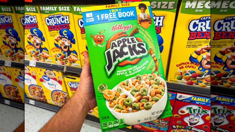 A hand holding a box of Apple Jacks cereal