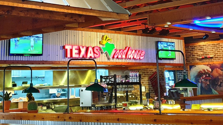 Interior of a Texas Roadhouse with a neon sign over the kitchen