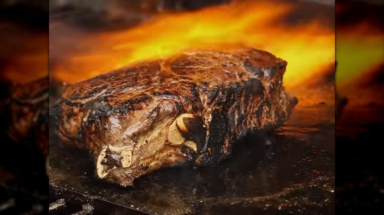 A large steak searing over a flaming grill