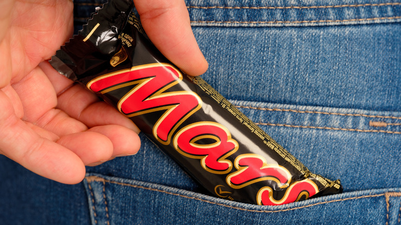 Hand grabs mars candy bar from jeans pocket
