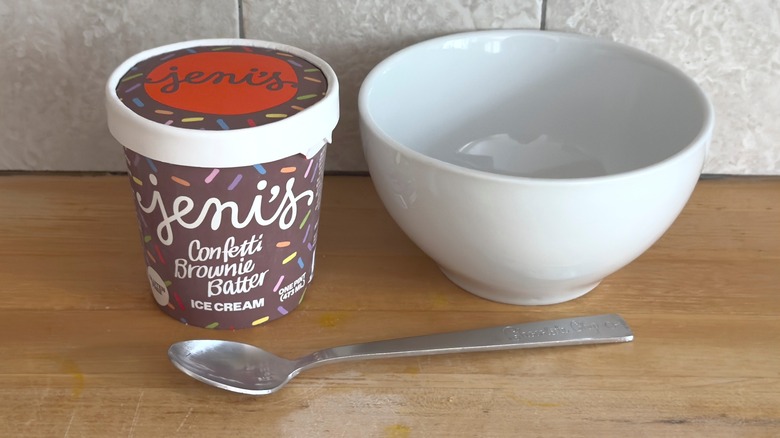 Tub of Jeni's Confetti Brownie Batter ice cream next to a spoon and bowl