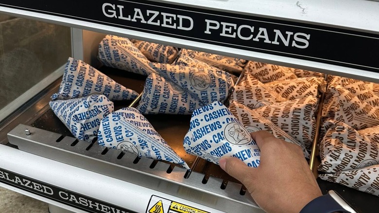 A hand reaching for a bag of glazed pecans from under the warmer at Buc-ee's