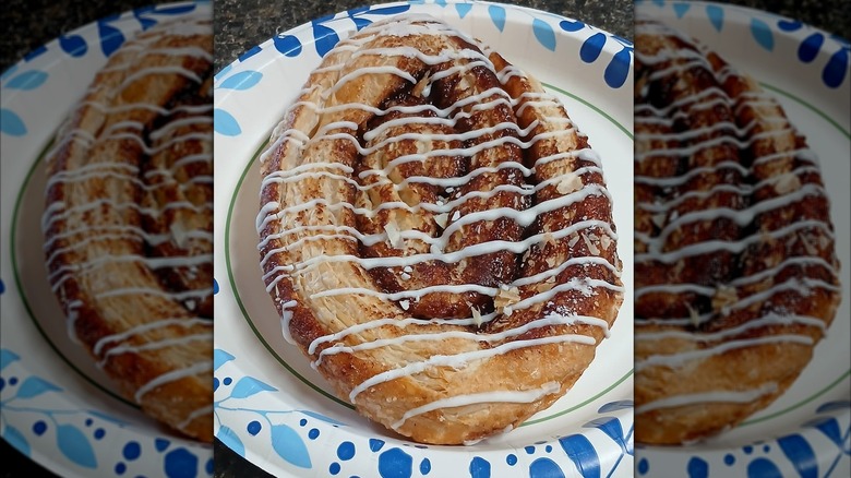 Oval-shaped cinnamon pastry with white icing drizzle on a paper plate