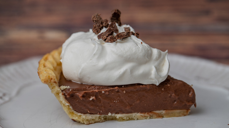 A slice of chocolate cream pie topped with whipped cream and chocolate bits on a white plate