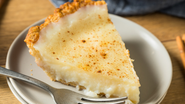 A slice of egg custard pie on a white plate placed on a wooden table