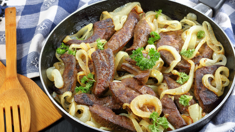 Old school liver and onions in a black plate, placed on a wooden table