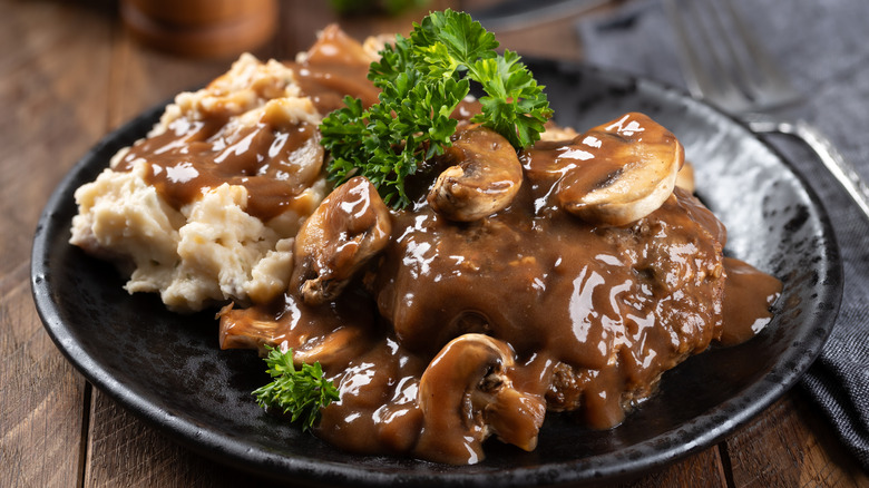 Salisbury steak topped with mushroom gravy and served with a side of mashed potatoes on a plate